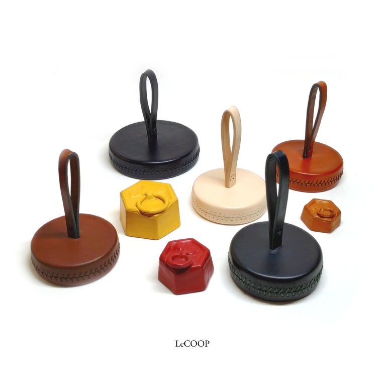 Pisapapeles de cuero con asa en negro, marrón y natural, y pesas hexagonales forradas en amarillo y rojo