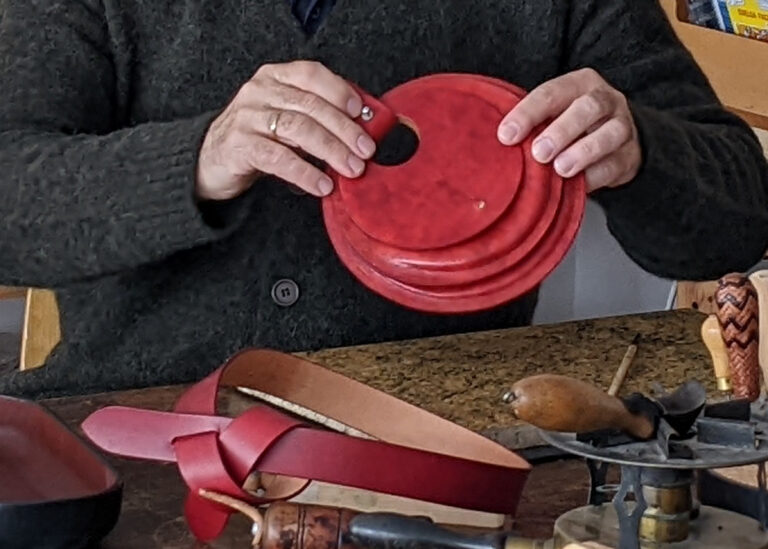 Víctor Montero sujeta un bolso circular de cuero rojo; sobre la mesa, cinturones del mismo color