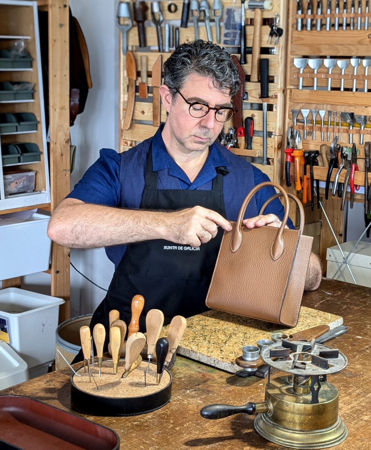 Víctor Montero en su taller sujetando un bolso de cuero color camel