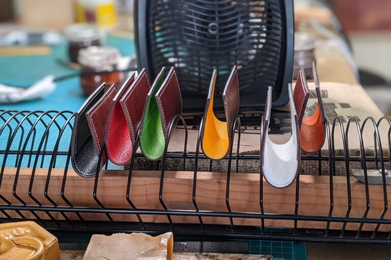 Tarjeteros de cuero con interior de colores secándose en una rejilla